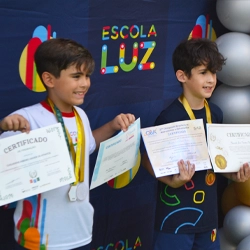 Alunos da Escola Luz recebendo medalhas e certificados pela participação nas Olimpíadas de Conhecimento (OBA, Bê-a-bá etc.)