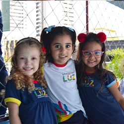 Três alunas da Escola Luz sorriem felizes durante o momento da acolhida