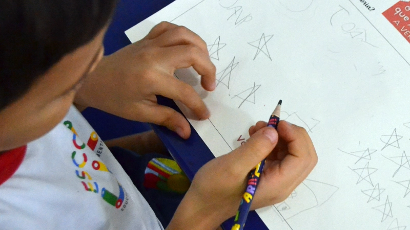 Criança pegando o lápis para escrever durante aula na Escola Luz